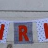 Mini vierkanten stoffen slinger voor Chris in de kleuren wit, donkergrijs en oranje.